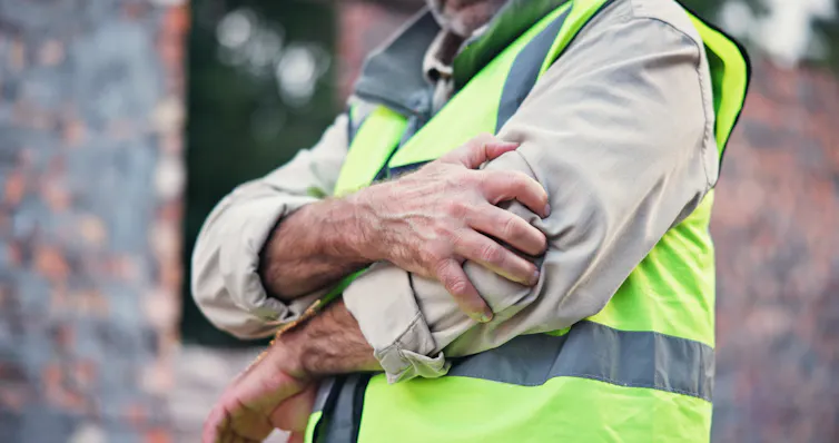 A man wearing a hi-vis vest holds his elbow in pain.
