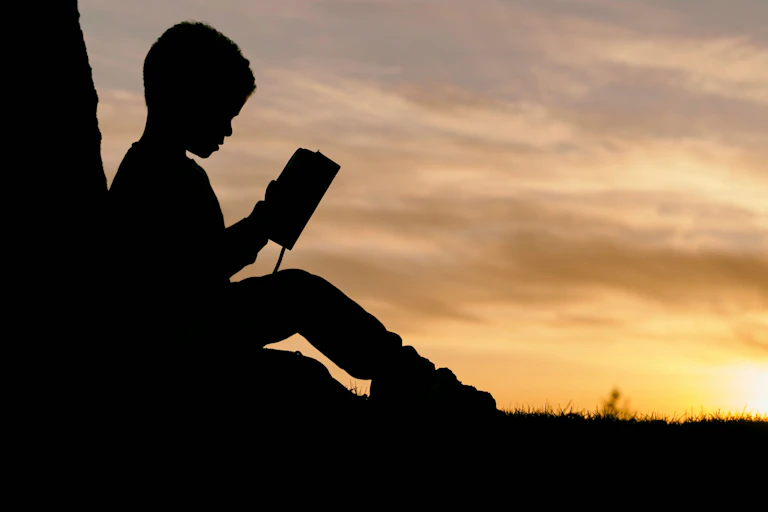 Silhouette of a seated child holding an open book