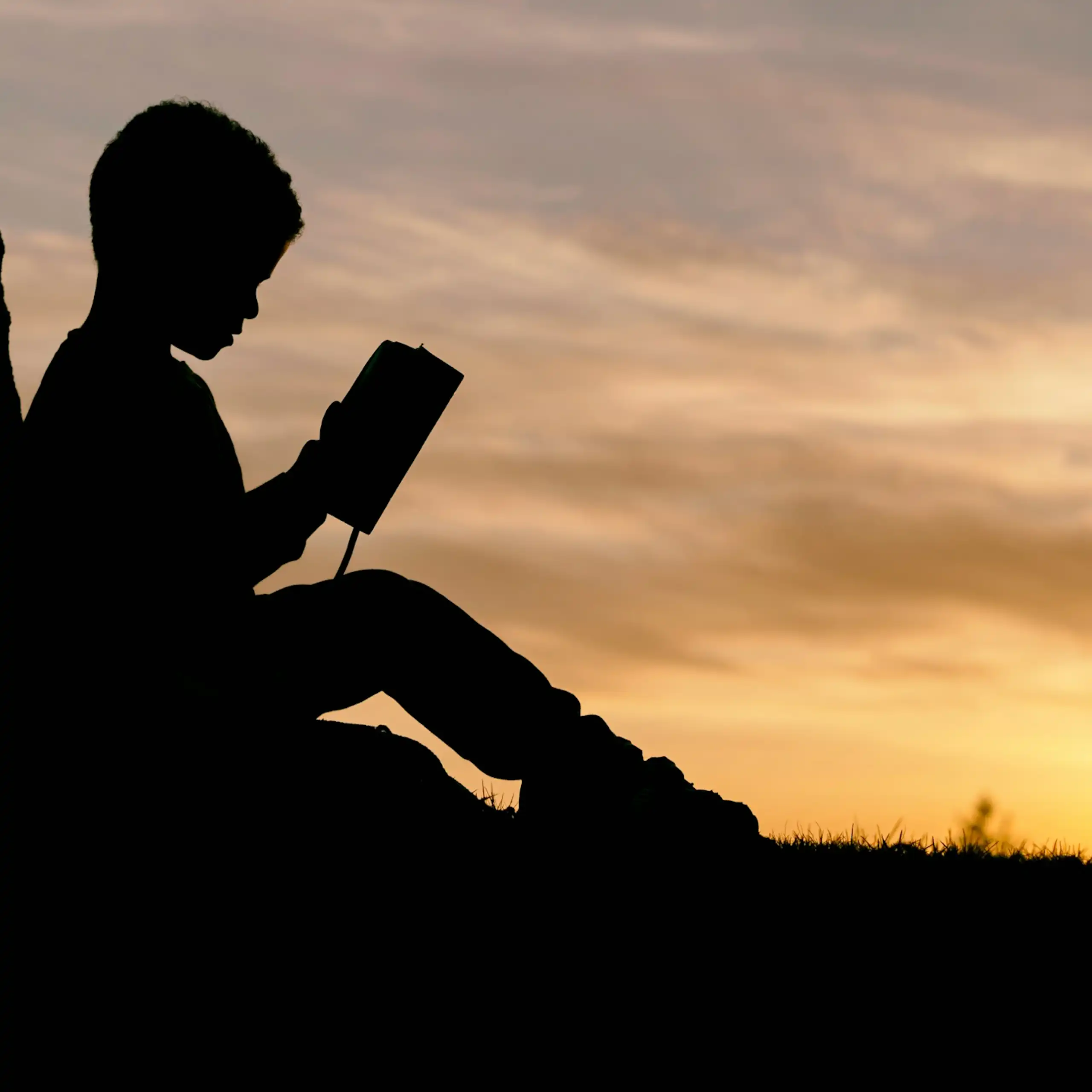 Silhouette of a seated child holding an open book