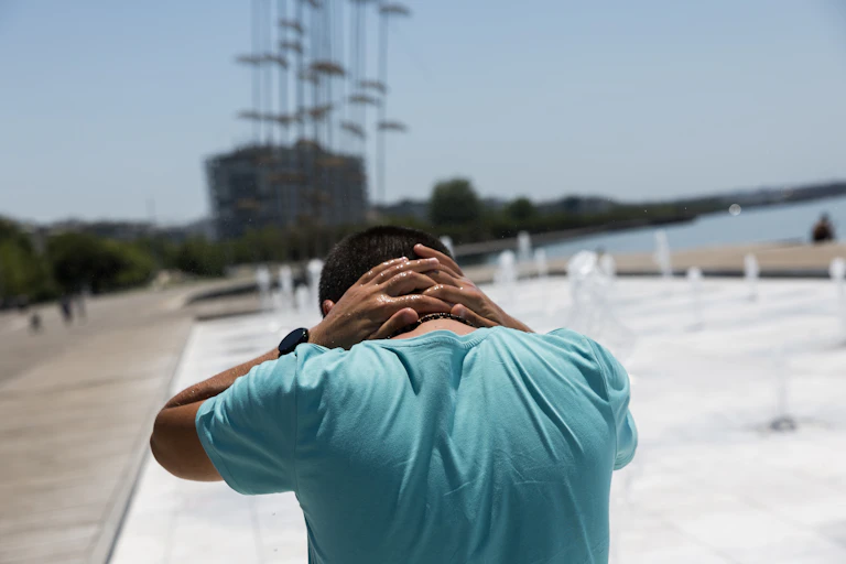 A man cools off at a fountain on a sunny day.