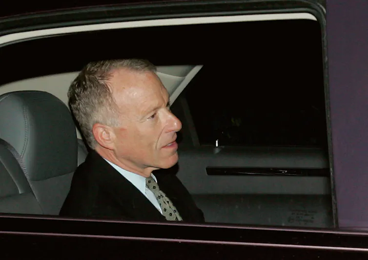 A man dressed in a suit and tie rides in the back seat of a car.