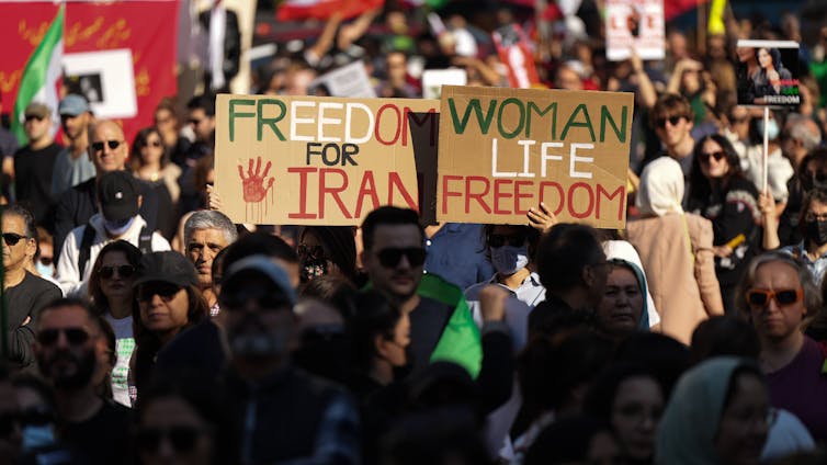Portada de personas, dos personajes sostienen en la multitud: uno lee 'Irán libre' otra 'mujer, vida, libertad'