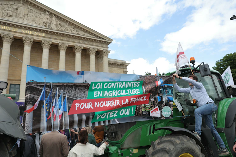 Des manifestants de la FNSEA et des jeunes agriculteurs déploient une banderole en faveur de la loi Duplomb devant l'Assemblée nationale, lors d'un rassemblement le 26 mai 2025.