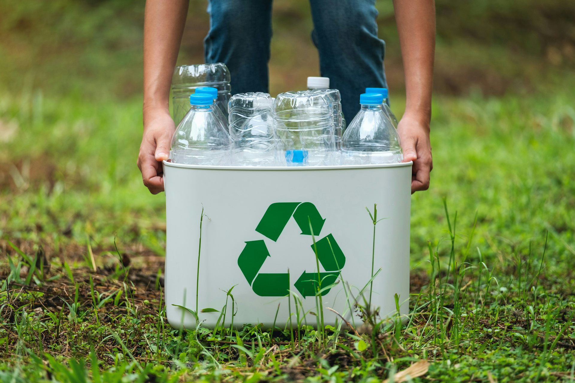 a close up of a person picking up a box with a green recycling triangle with plastic bottles inside