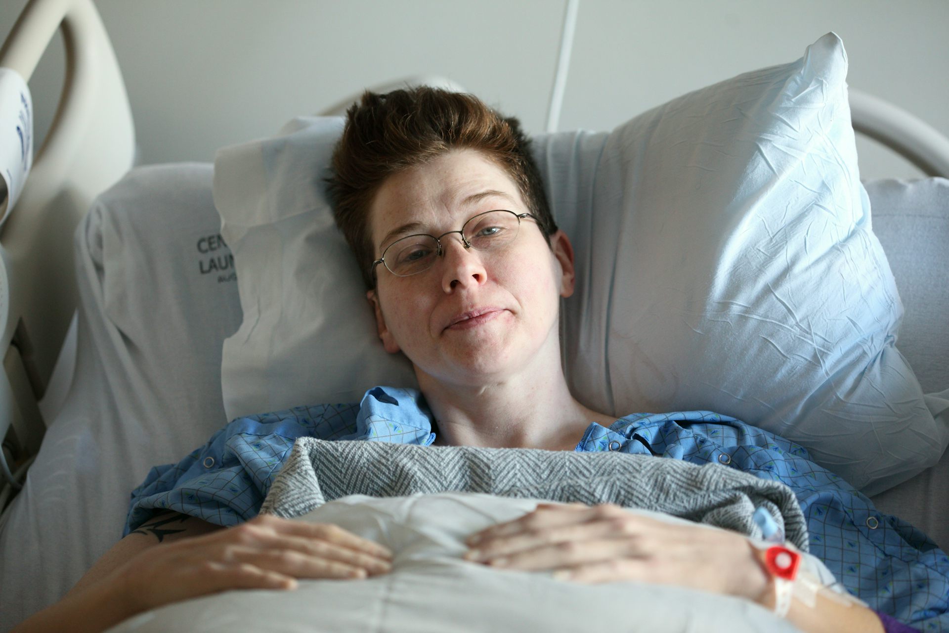 A woman lies in a hospital bed. she smiles slightly