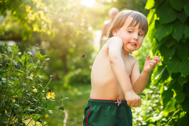 Little boy boy dodges flying bumblebee in garden in summer