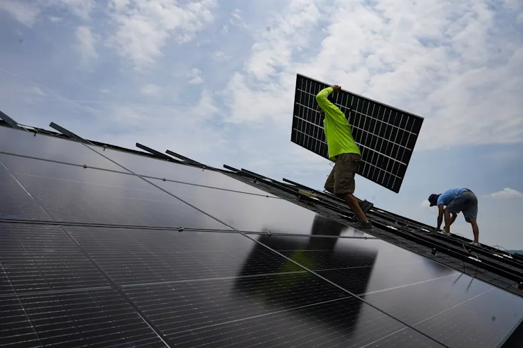 Workers install solar panels on a roof.