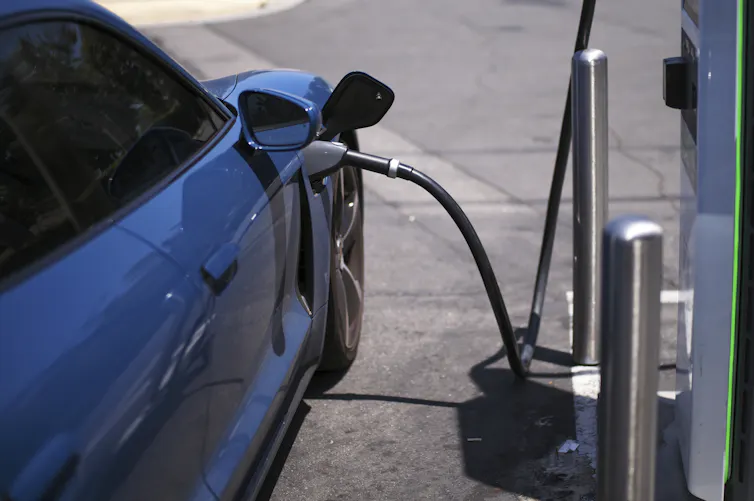 A car connects to a large metal box with a thick cable.