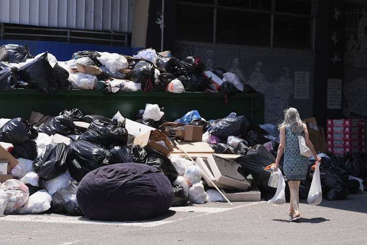 Como la huelga sanitaria de Filadelfia difería de las disputas laborales pasadas en la ciudad 4 Una mujer que se muestra desde la espalda usada por las bolsas de basura mientras camina hacia una enorme pila de basura.