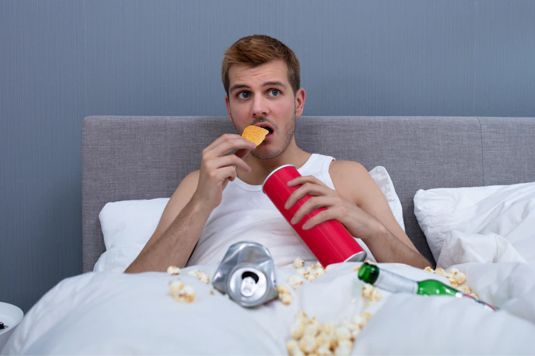Un homme mange des chips dans un lit sale.