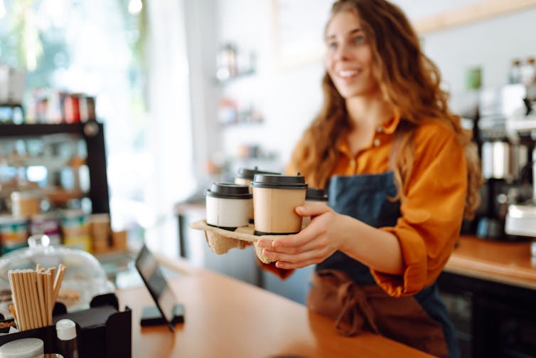 A cafe worker with long hair holds coffee cups with lids