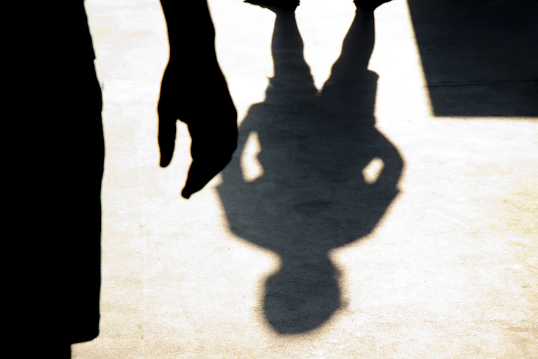 A shadow of a child on the ground and a silhouette of a person's hand