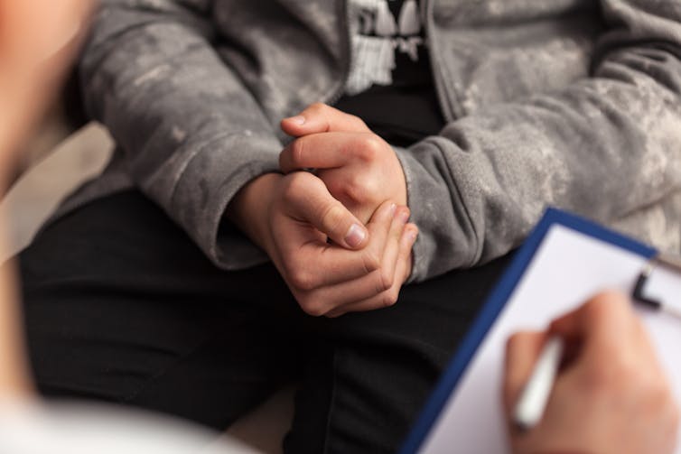A close up of a teenage boys hands clasped together in a counselling session