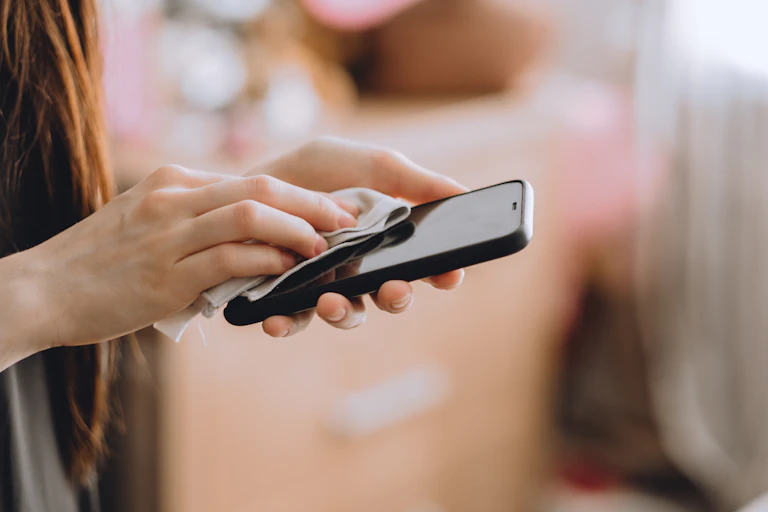 A woman wiping down her smartphone with a soft cloth.
