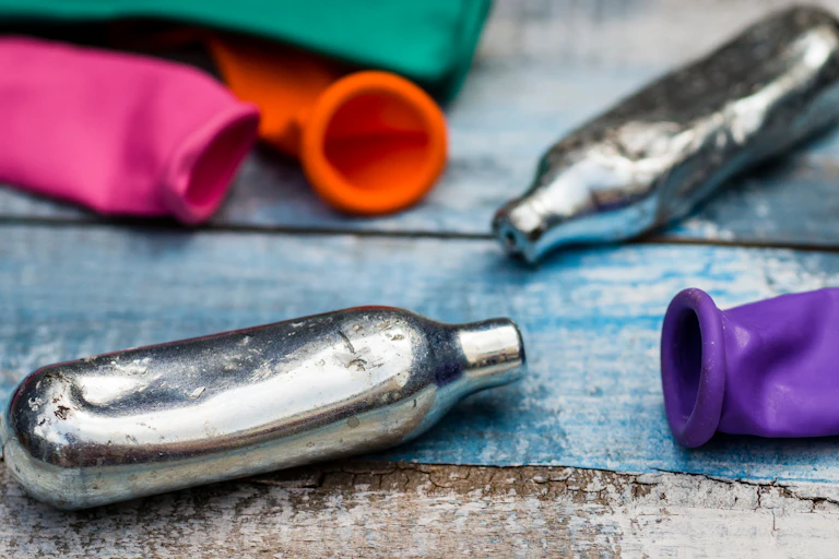Des cartouches de protoxyde d’azote vides, posées à côté de ballons de baudruche utilisés pour inhaler le gaz.