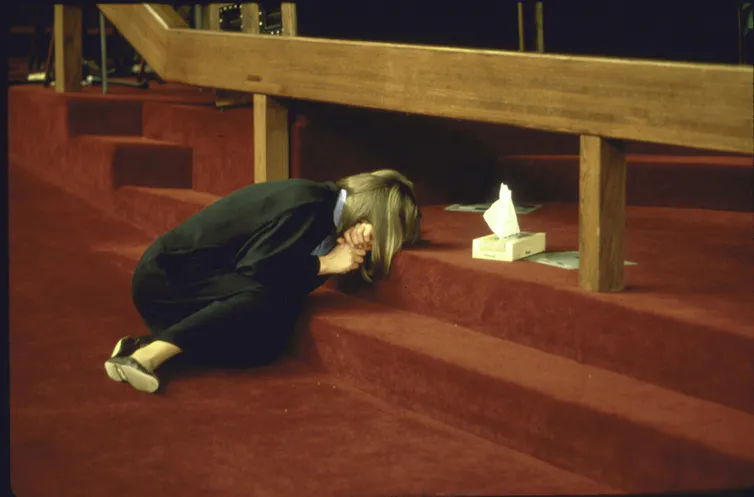 A woman lying curled up on carpeted steps with her head in her arms.