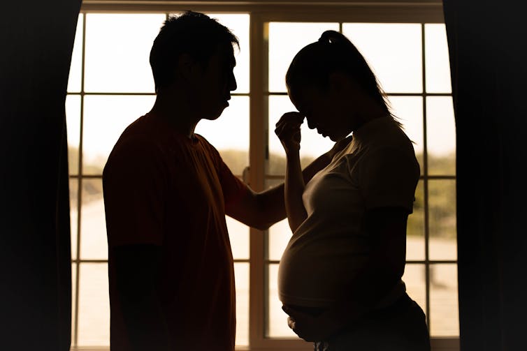 Man and pregnant woman silhouetted, looking stressed