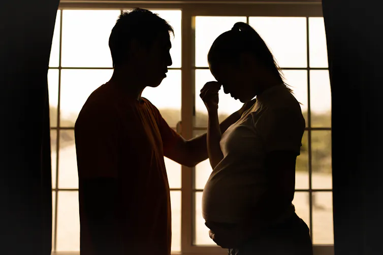 Man and pregnant woman silhouetted, looking stressed