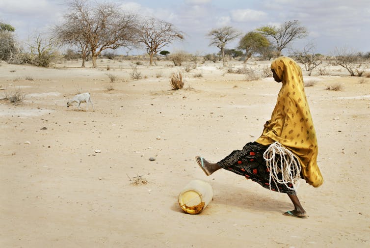 woman in africa dress pushes jerrycan along desert in drought