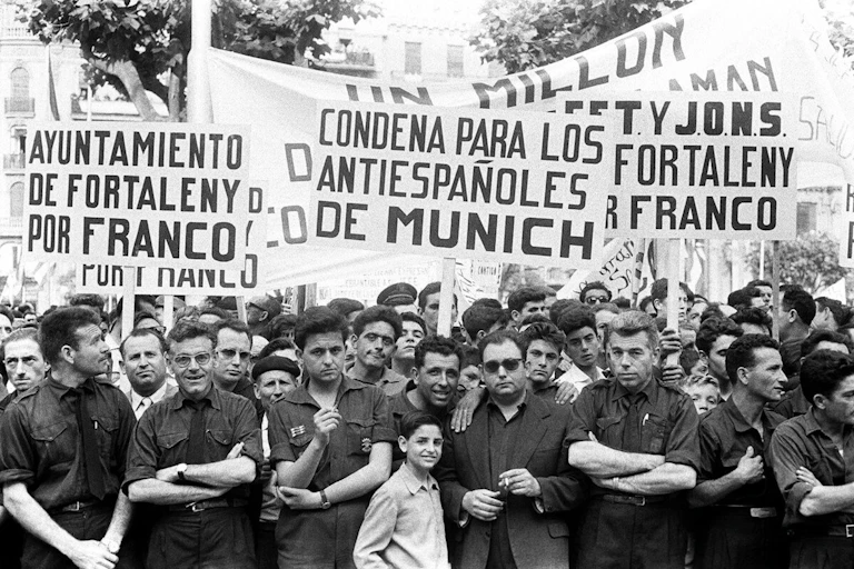 Un grupo de señores y niños portan carteles que ponen "condena para los antiespañoles de Múnich".