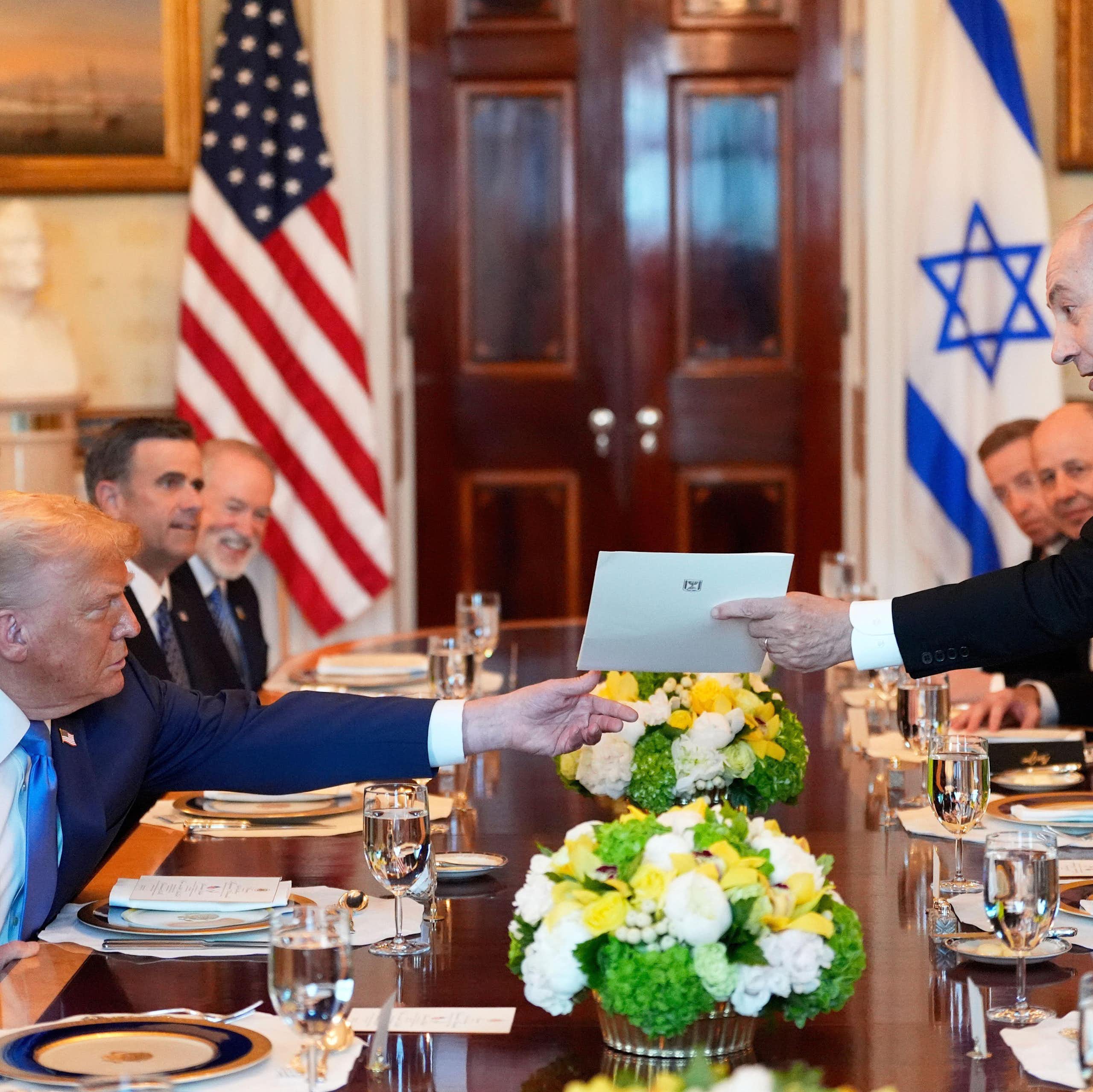 Israeli prime minister, Benjamin Netanyahu, hands a letter to the US president, Donald Trump, over a table set for dinner.