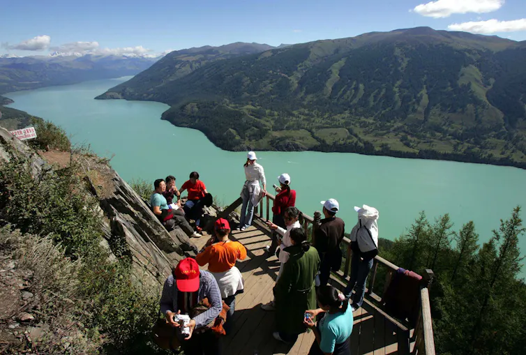 People stand on a wooden platform on a mountain overlooking a lake