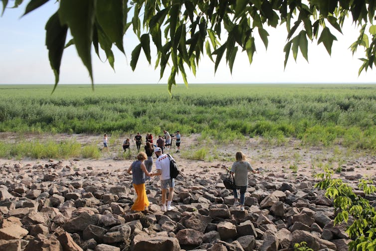 People walk through an area of rocks to a grassy plain.