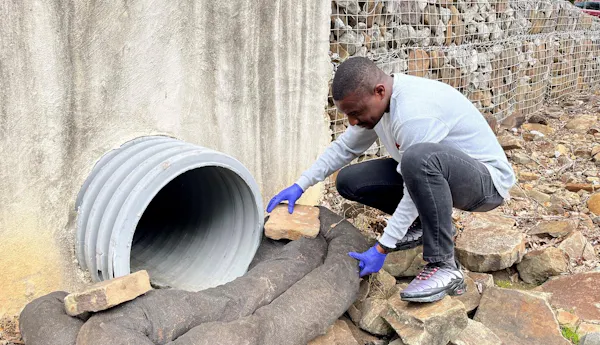 Un hombre coloca tubos flexibles llenos de biochar debajo de un desagüe pluvial.