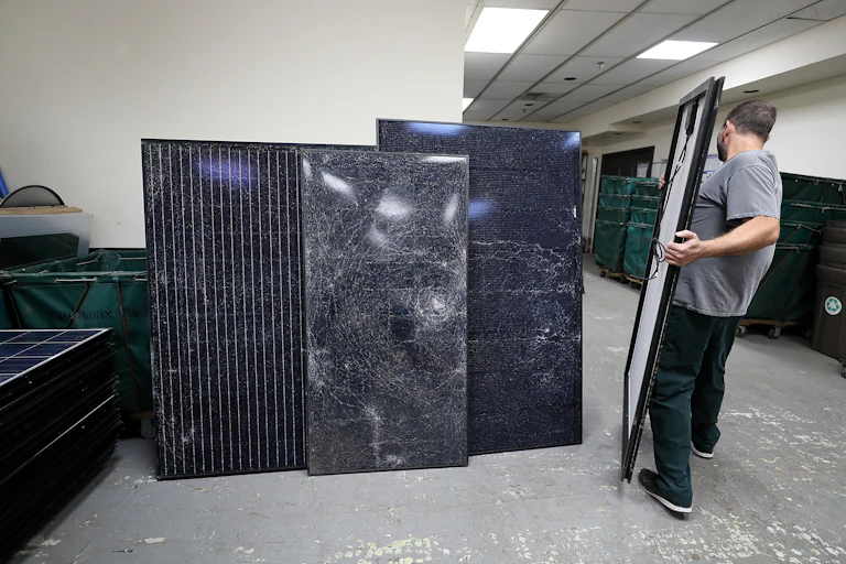 A person carries a large black rectangular object down a hallway lined with similar items.