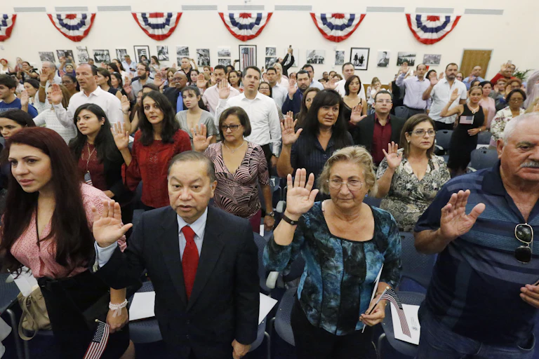 Dozens of people lift their right hands in the air as they recite an oath.