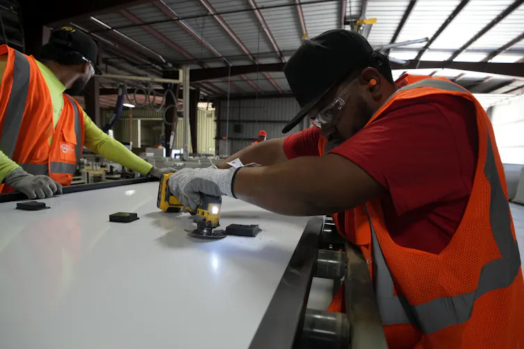 People in reflective vests and protective clothing use tools to take apart a large item.