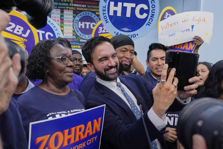 A bearded young man takes selfies with a group of people.