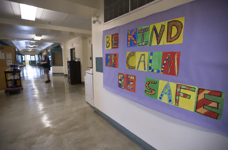 A bulletin board says 'be kind, be safe' in a school hallway.
