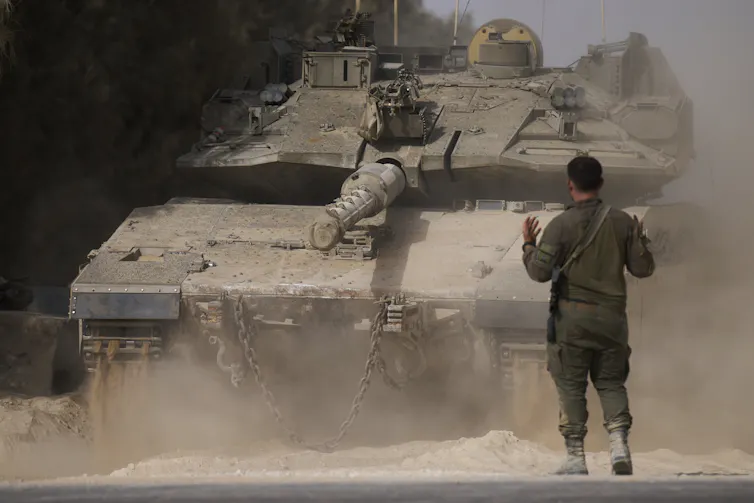 A man stands in front of an Israeli tank in Gaza