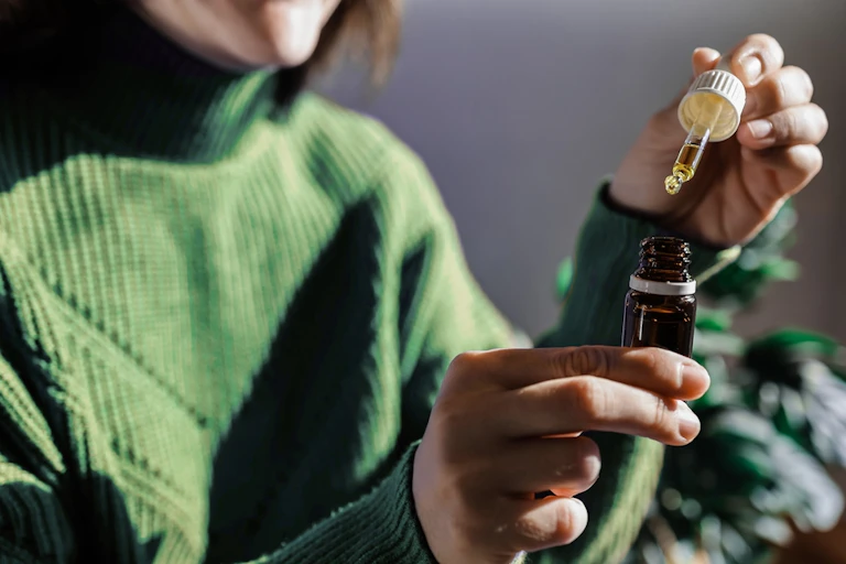 Woman holding dropper of medicinal cannabis oil in one hand, bottle in another