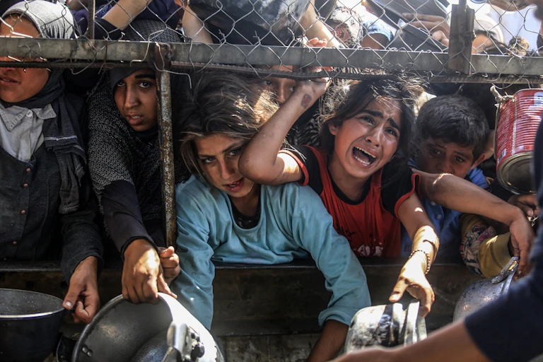 Several children pleading for food from behind a wire fence in Gaza.