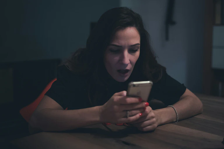 A woman in shock looks at her phone in a darkened room