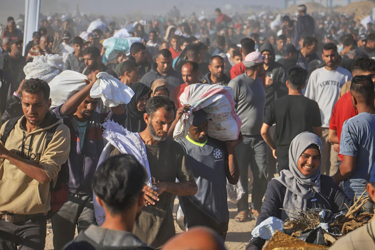 A huge crowd of Palestinian people carry their belongings along a dusty road.