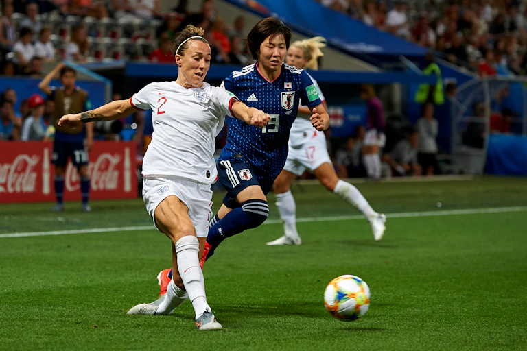 England footballer Lucy Bronze faces off with an opponent on the pitch, both trying to get the ball.