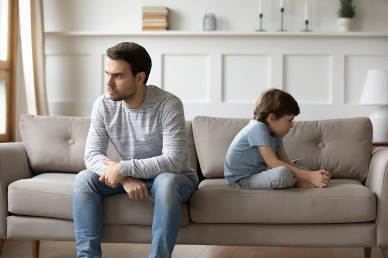Padre e hijo sentados en un sofá dándose la espalda sin hablar