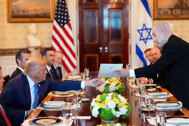 Israeli prime minister, Benjamin Netanyahu, hands a letter to the US president, Donald Trump, over a table set for dinner.