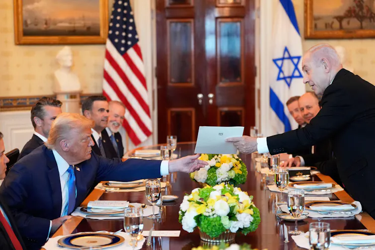 Israeli prime minister, Benjamin Netanyahu, hands a letter to the US president, Donald Trump, over a table set for dinner.