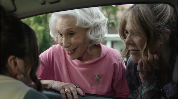 Two older women looking in a car window at a young woman and smiling.