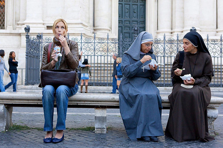 Una mujer come un helado en un banco al lado de dos monjas que hacen lo mismo.