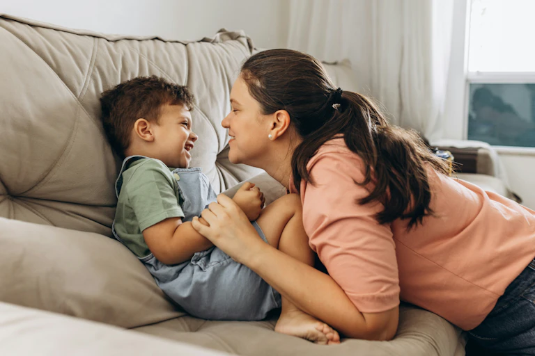 A mother cuddles and smiles with a young boy.