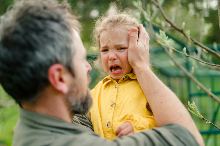 A bearded father holds a sobbing child.