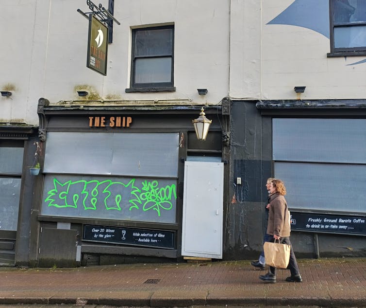 A woman walks past a boarded up pub called The Ship