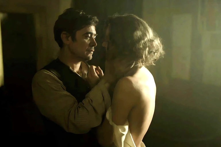 A man and a woman in a dimly lit bedroom embracing.