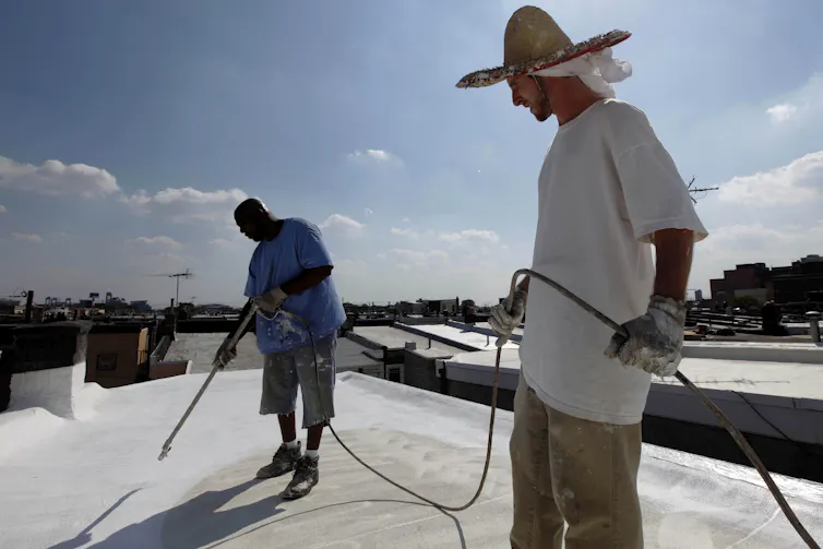 Two workers apply paint to a flat roof.