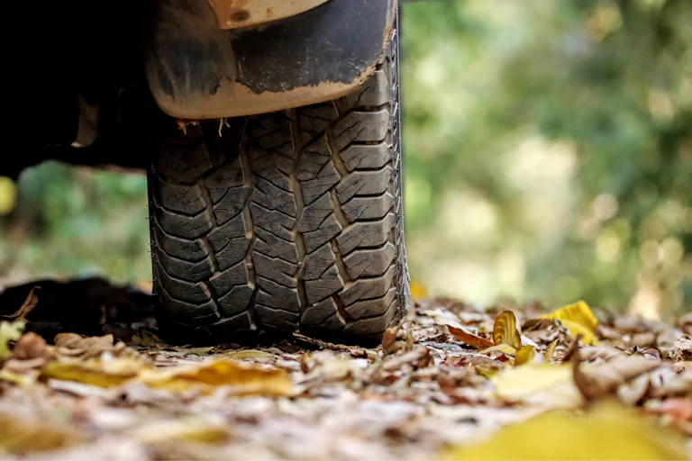 A vehicle with a closeup of the tire on a road with leaves.
